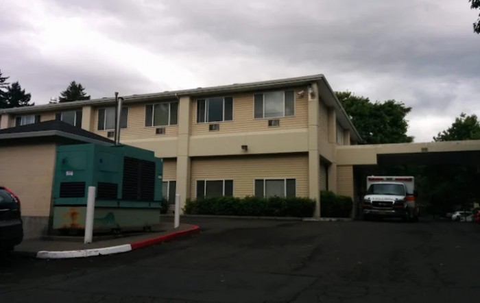 A two-story building with a parking lot in front under a cloudy sky.