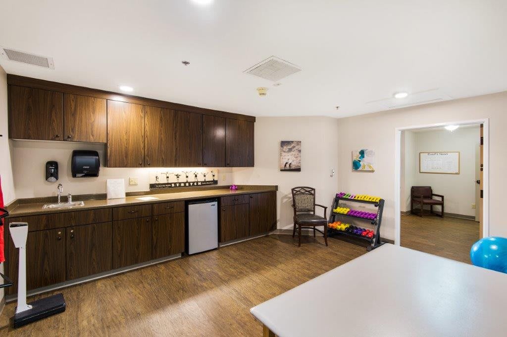 A modern kitchen interior featuring wood cabinetry, a small refrigerator, and artwork on the walls.