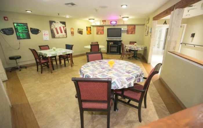 A cozy dining room with several tables and chairs, decorated with vibrant tablecloths and wall art.