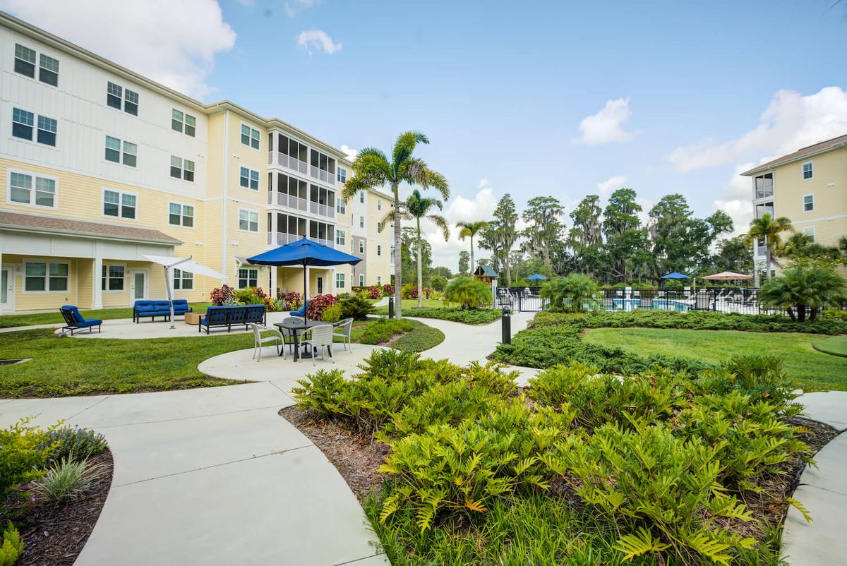 A well-landscaped outdoor area with a pathway, seating, and palm trees near a multi-story building.