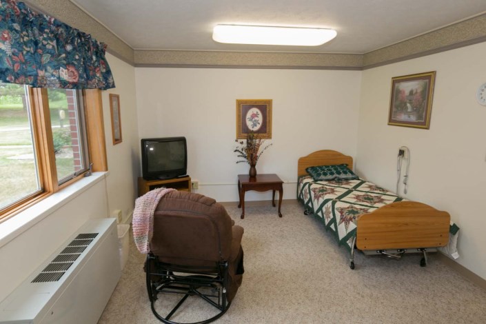 A simple bedroom with a single bed, chair, and television.