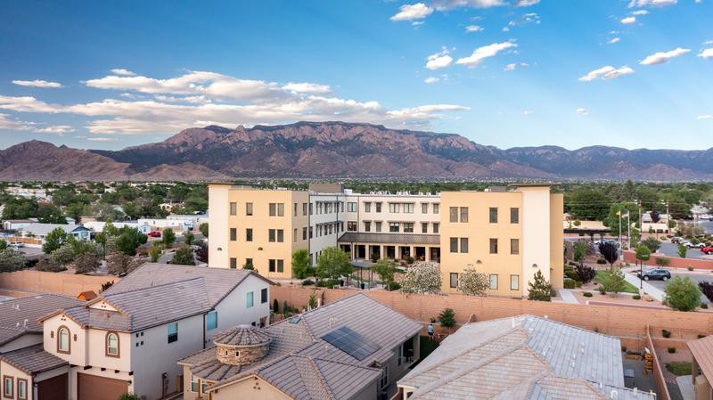 A picturesque view of a residential building set against a backdrop of majestic mountains under a clear sky.