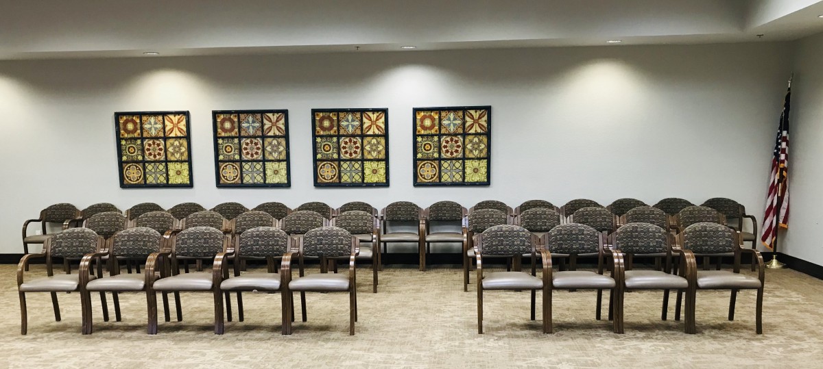 A waiting room with multiple rows of chairs and quilt pattern artwork on the wall.
