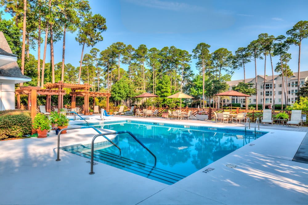 A serene outdoor swimming pool area surrounded by trees and patio seating, ideal for relaxation.
