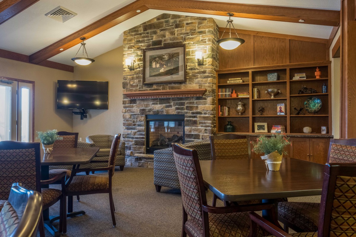 A cozy living room with a stone fireplace, wooden beams, and a built-in library.