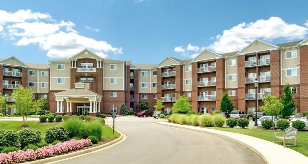 A modern residential apartment complex surrounded by landscaped greenery under a partly cloudy sky.