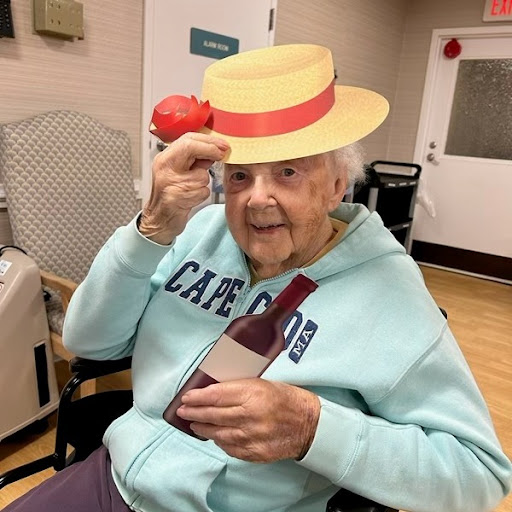 An elderly woman wearing a stylish hat enjoys her time at a gathering, holding a wine bottle.