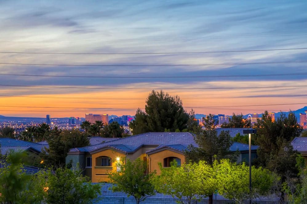 A serene suburban sunset with a view of houses and trees under a colorful sky.