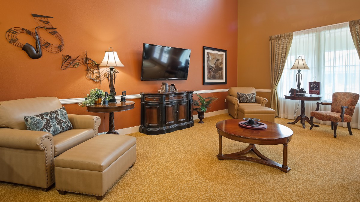 A cozy living room with orange walls, featuring a TV, comfortable seating, and tasteful decor.