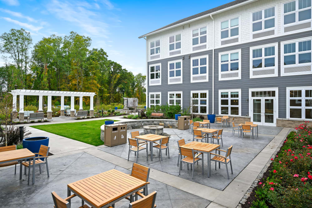 A modern apartment patio area with tables and chairs, surrounded by greenery.