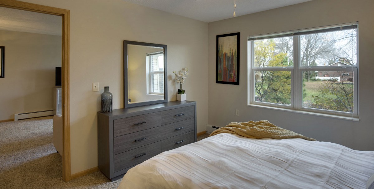A cozy bedroom featuring a dresser with a mirror, decorated with plants and artwork.