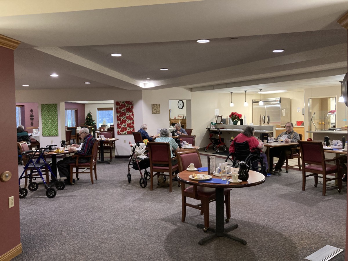 A community space in a nursing home with seniors sitting at tables.