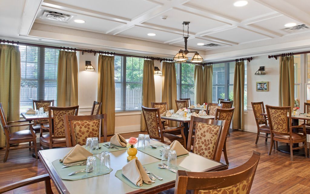 A well-decorated dining area with neatly arranged tables and chairs, featuring elegant lighting and large windows.