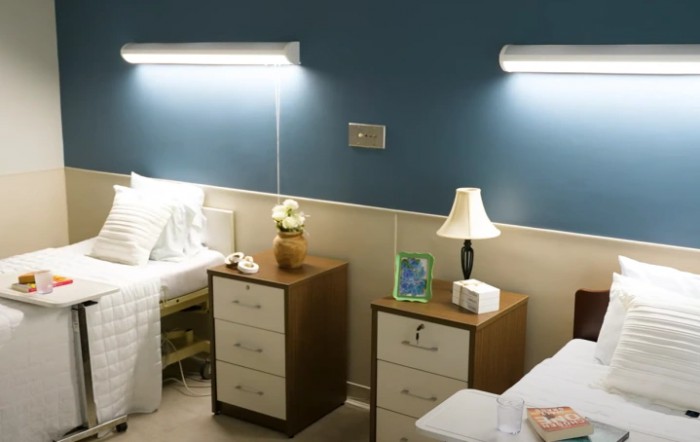 A hospital room featuring two beds with nightstands and lamps.