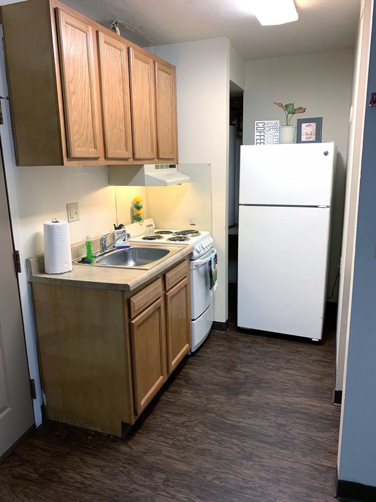 A compact apartment kitchen with wooden cabinets, a refrigerator, and a stove.