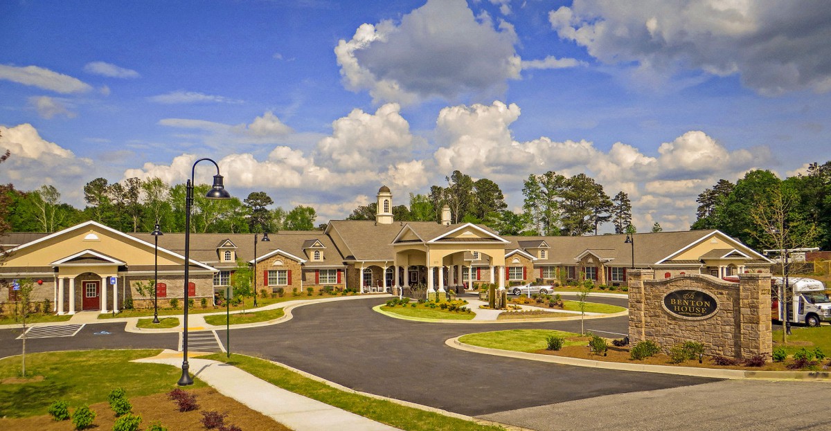 A picturesque view of a large residential building with elegant architecture, surrounded by landscaping and trees under a partly cloudy sky.