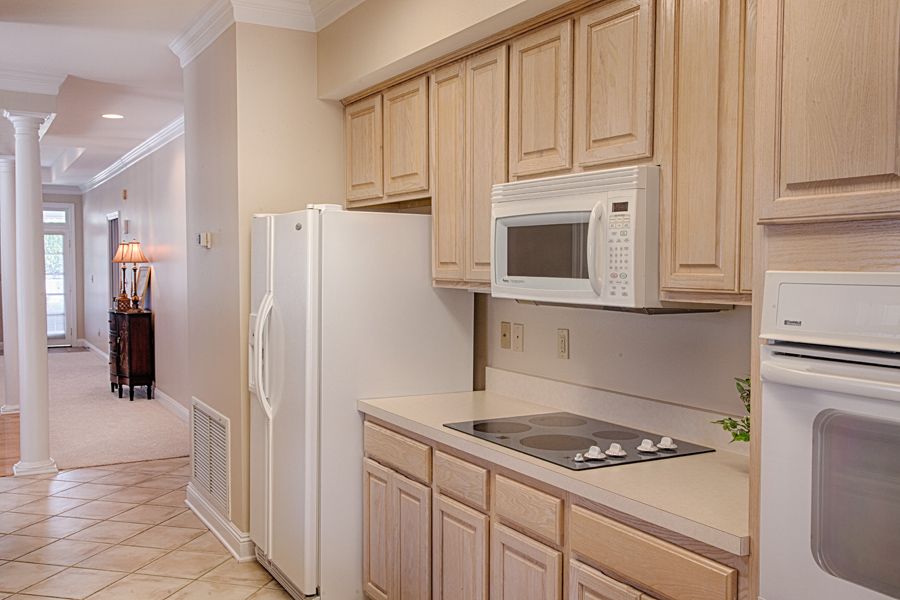A modern kitchen with light wood cabinets, a white refrigerator, microwave, and electric stovetop.