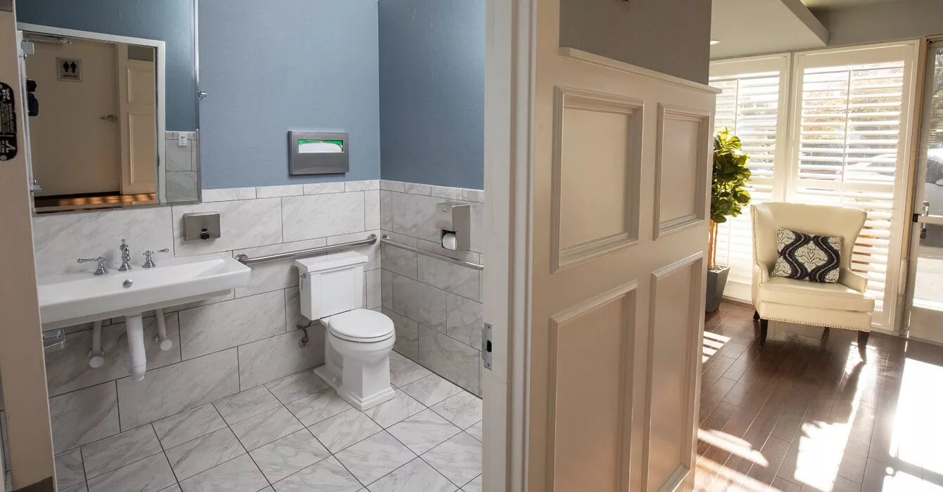 A modern bathroom with a white tiled floor and blue walls, featuring a toilet and an open door.