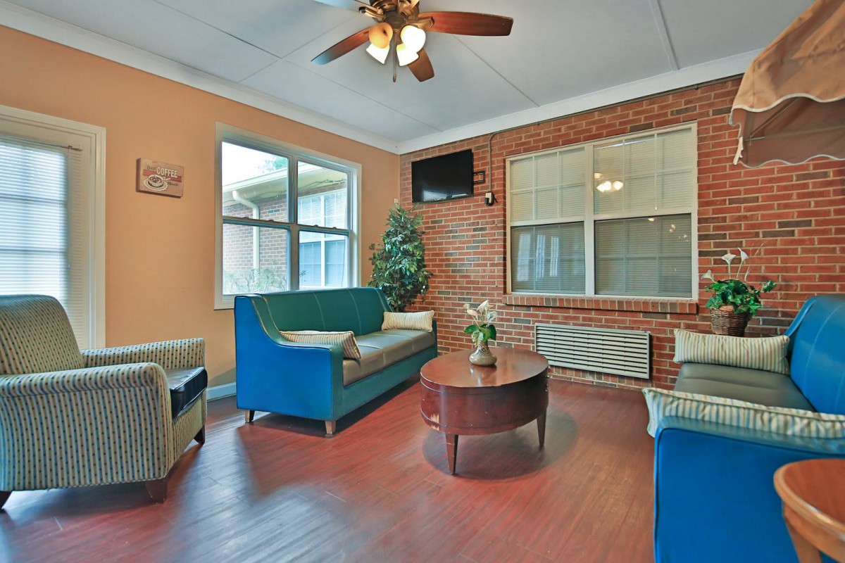 A cozy living room with colorful sofas, a round coffee table, and natural light streaming in through the window.