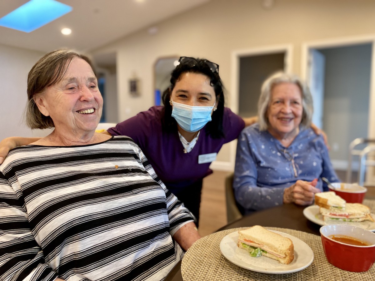 Three people smiling and sharing a meal together indoors.