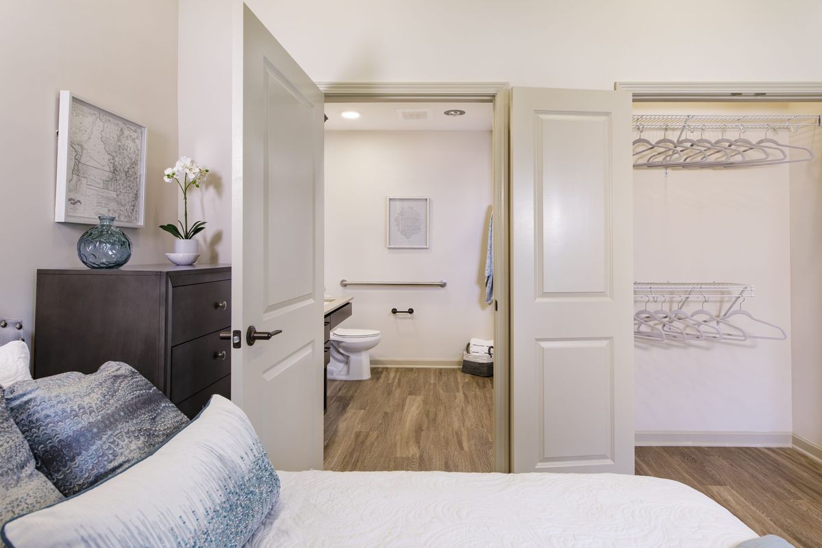 A modern bedroom with a view into an adjacent bathroom, featuring neutral tones and sleek furnishings.