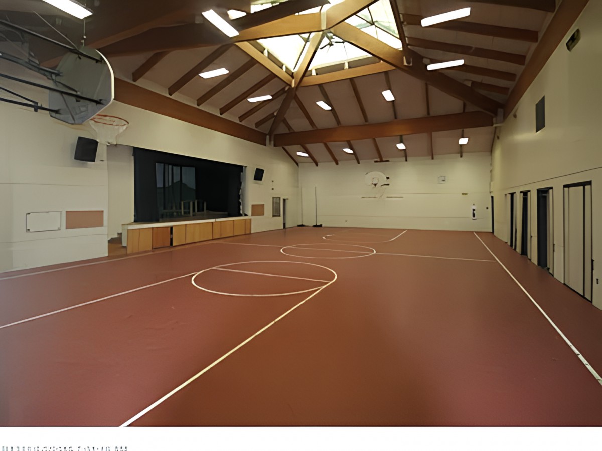 An empty indoor gymnasium with a basketball court and wooden ceiling beams.