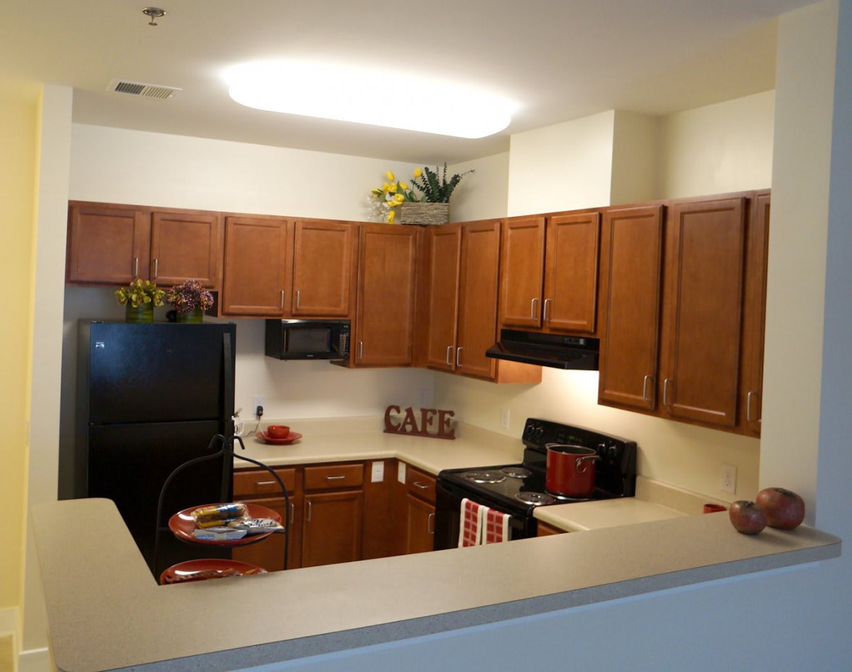 Modern apartment kitchen with wooden cabinets and black appliances.