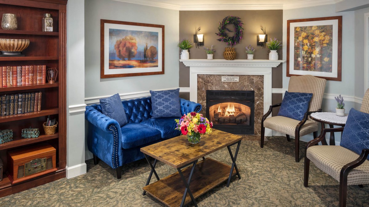 A cozy living room featuring a blue sofa, rustic coffee table, and a warm fireplace adorned with artwork and decor.