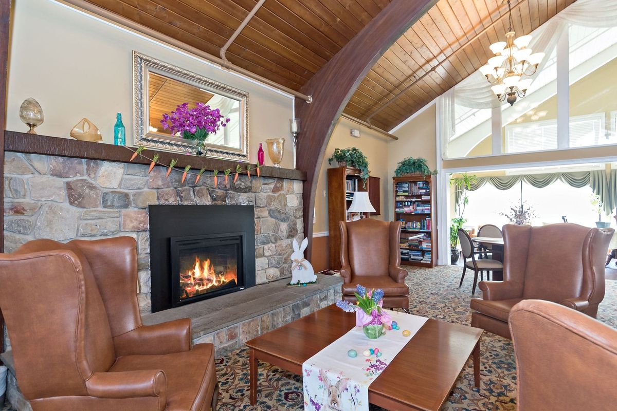 A cozy living room featuring a stone fireplace, leather chairs, and wood ceilings.