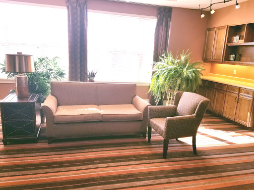 A cozy living room setup featuring a couch and an armchair, complemented by plants and abundant natural light.