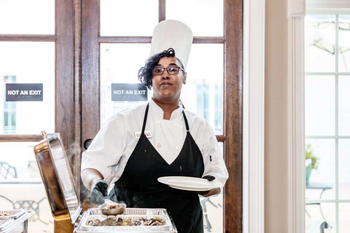 A chef in uniform carrying a plate of food.