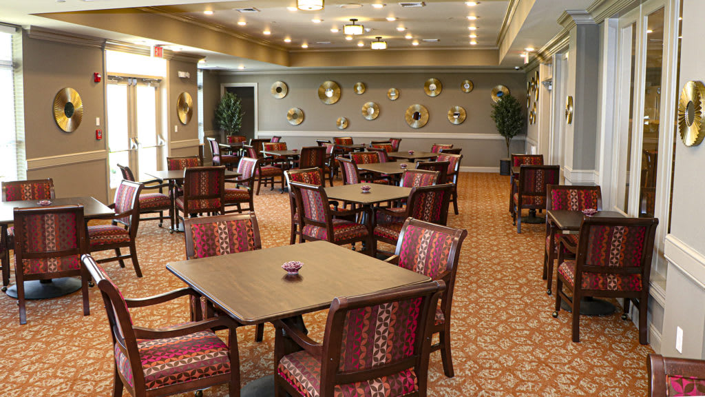 An elegant dining area with neatly arranged tables and chairs, featuring decorative wall art and a carpeted floor.