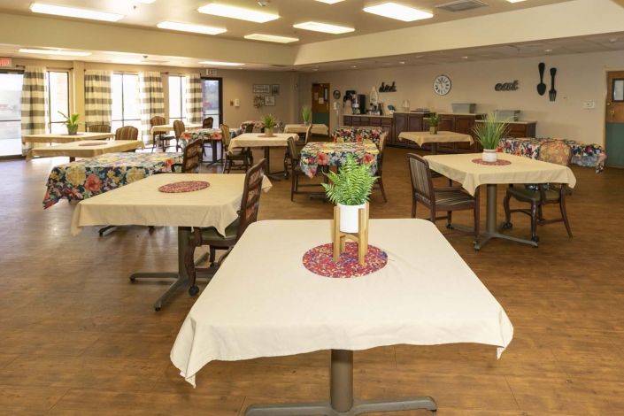 An indoor dining area with neatly arranged tables and chairs, decorated with potted plants.