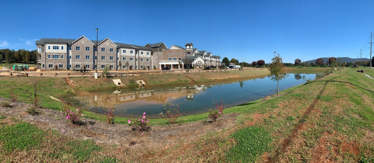 A scenic view of buildings reflected in a tranquil lake under a clear blue sky.