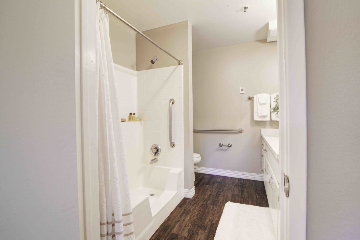 A clean and modern bathroom with a shower tub combination, featuring a curtain, grab bars for safety, and neatly arranged towels.