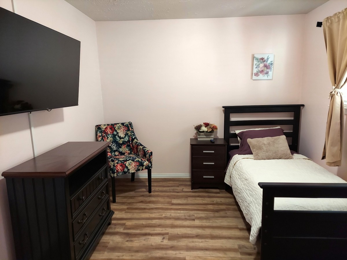 A cozy bedroom with a neatly made bed, a dresser, and a TV mounted on the wall.