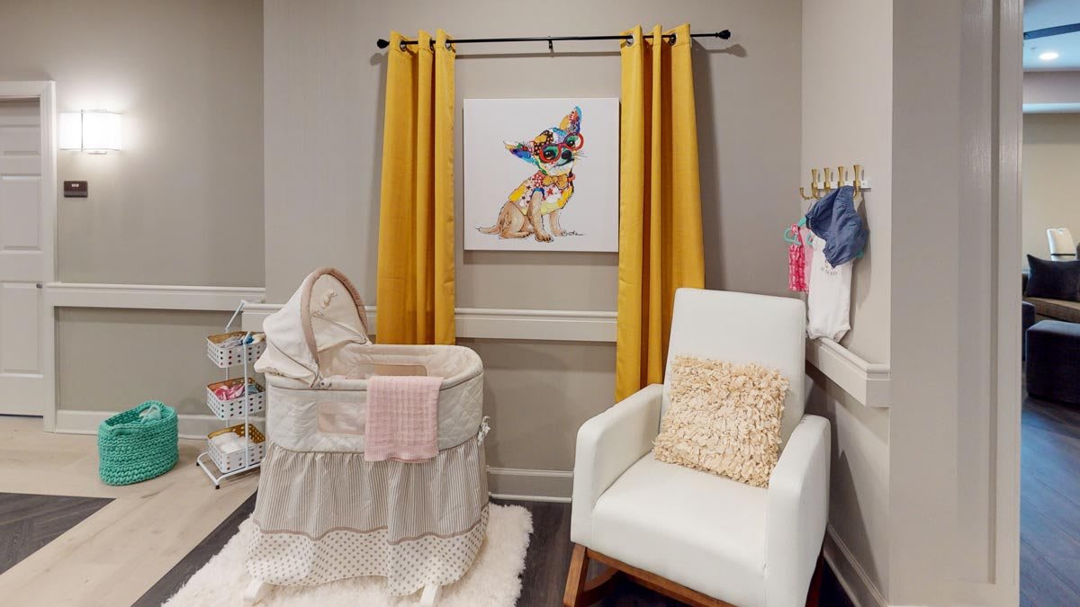 A cozy nursery featuring a bassinet, rocking chair, and colorful artwork with bright yellow curtains.