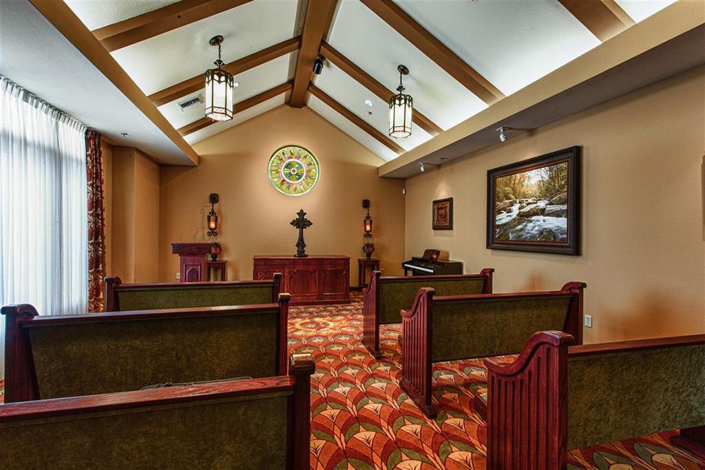 An interior view of a chapel featuring rows of pews and an altar under a vaulted ceiling with wooden beams.
