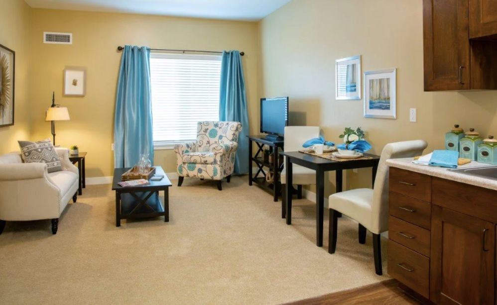 A cozy living room with a dining area, featuring a patterned chair, blue curtains, and a small TV.
