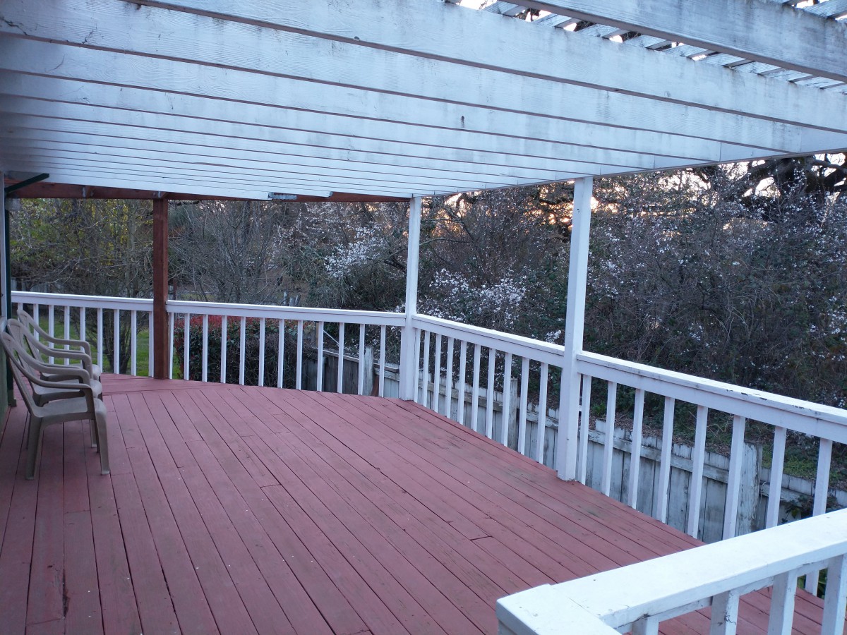 A wooden deck with a pergola and railing, captured during sunset.