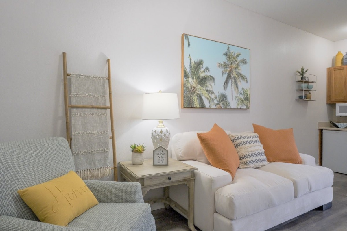 A cozy living room with a white sofa, colorful pillows, and tropical artwork on the wall.