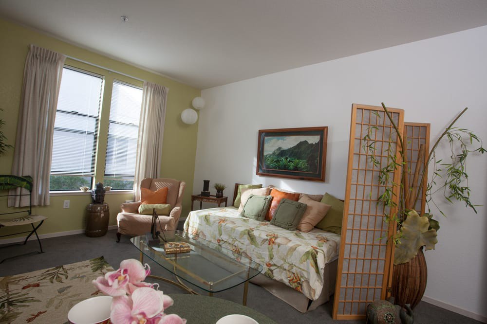A cozy living room with a sofa, armchairs, and a coffee table, decorated with cushions and a painting on the wall.