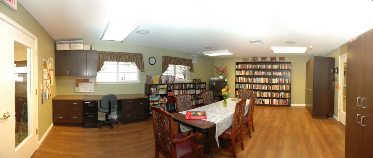 A cozy library with bookshelves, a large table for reading, and an office desk.
