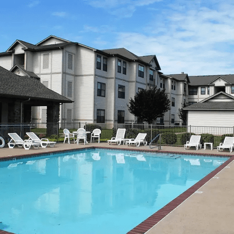 An outdoor swimming pool surrounded by lounge chairs with an apartment building in the background.