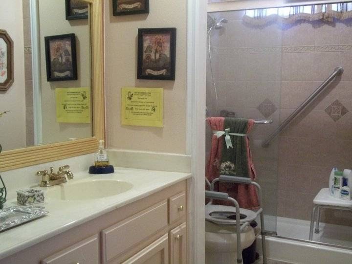A bathroom featuring a sink with a mirror, a shower equipped with a handrail, and various framed pictures and safety signs on the wall.