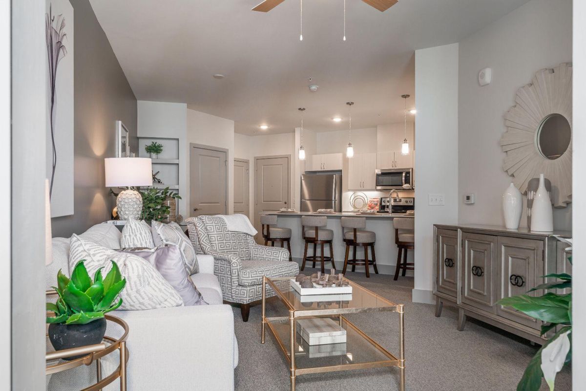 A modern open-concept living space featuring a cozy living room with a sofa and coffee table, adjacent to a sleek kitchen with bar stools.