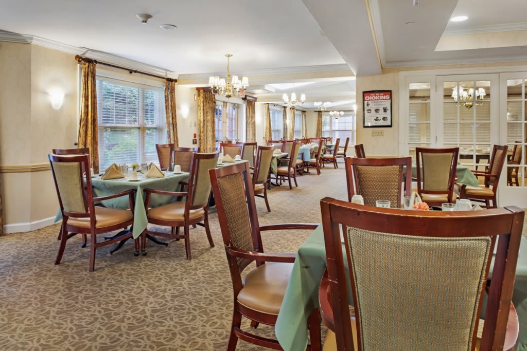 An elegant dining area with neatly arranged tables and chairs, complemented by warm lighting and large windows.