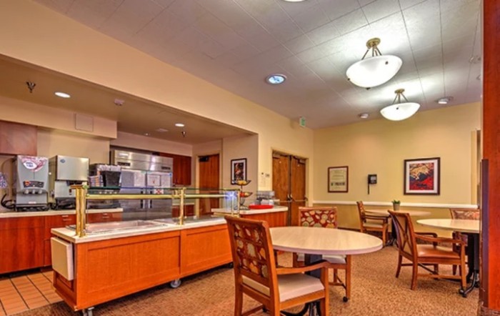 An interior view of an empty cafeteria with tables, chairs, and a food service counter.