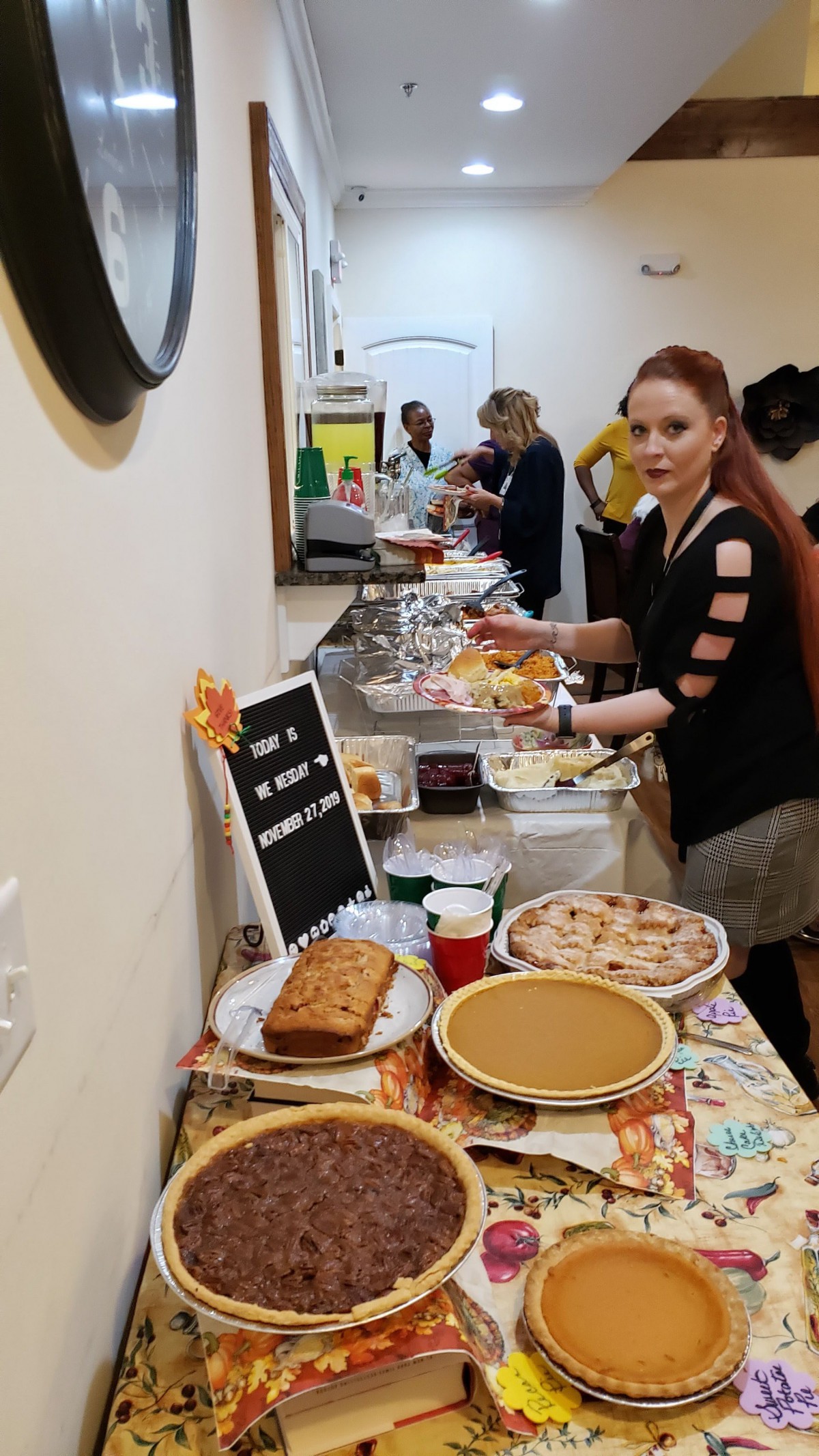 A group of people enjoying a potluck with a variety of desserts and dishes laid out on a table.