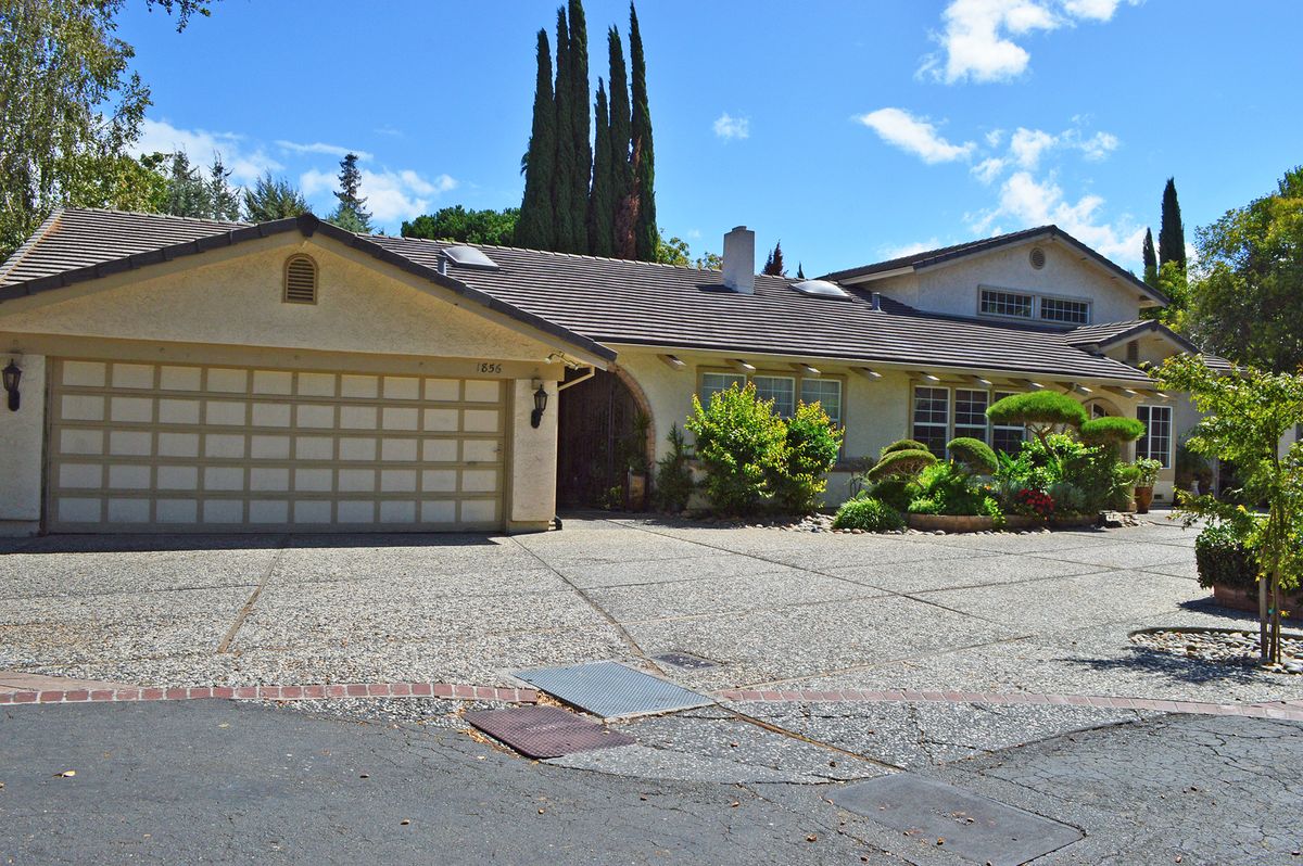 A suburban house with a large driveway and garage, surrounded by greenery under a clear blue sky.